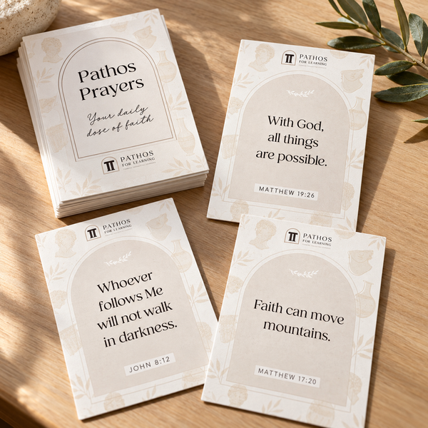 Pathos Prayer Cards arranged and stacked on a warm wooden desk with an olive branch.
